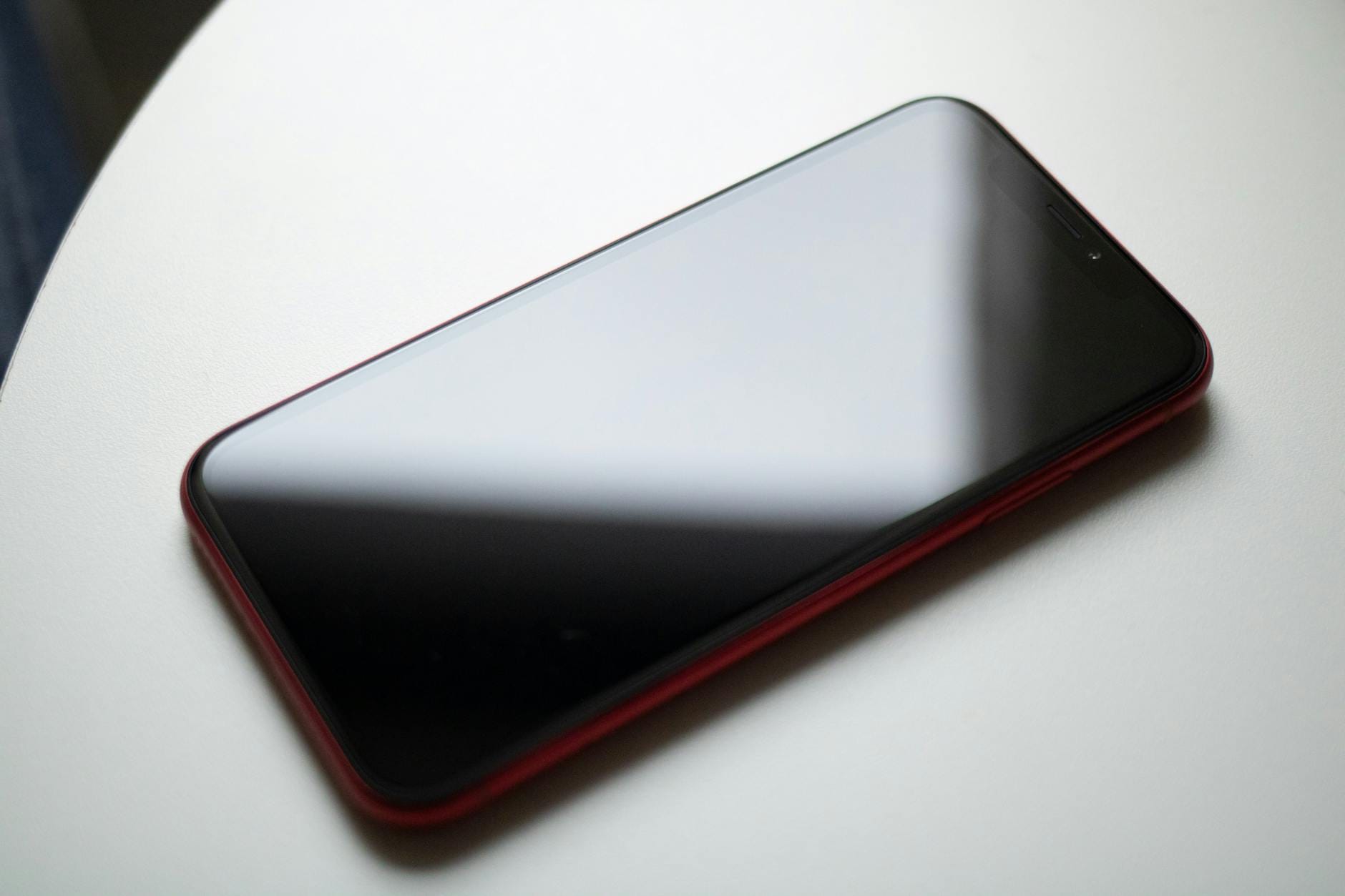 Czerwony smartfon leżący na białym stole przed naklejeniem szkła hartowanego