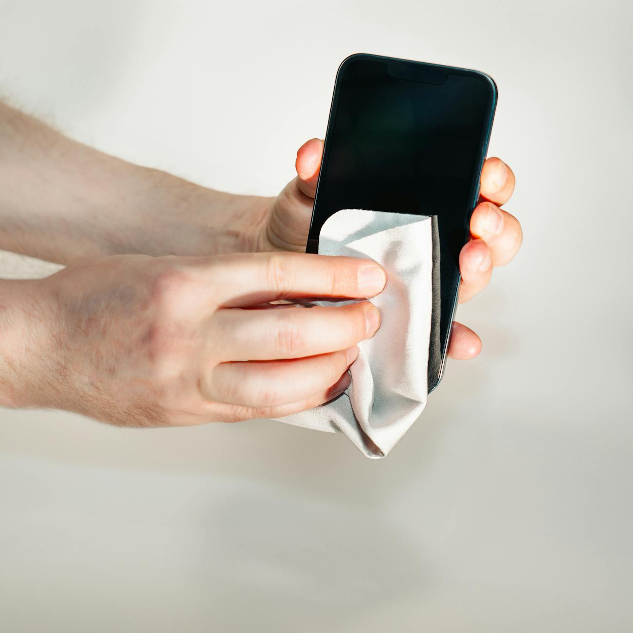 Dłonie czyszczące ekran smartfona miękką ściereczką przed naklejeniem szkła