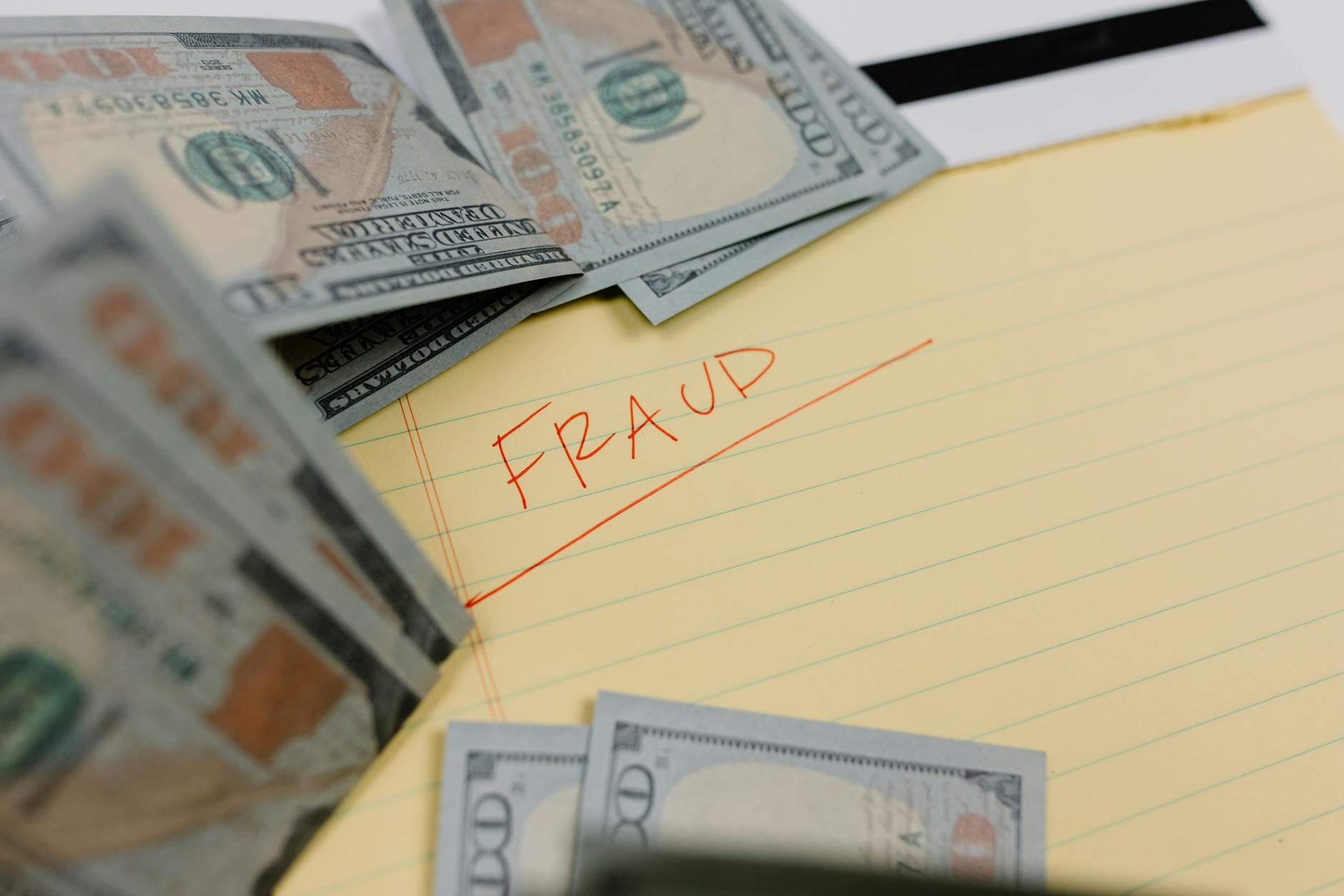 Zbliżenie na banknoty dolarowe z napisem fraud na żółtej karteczce