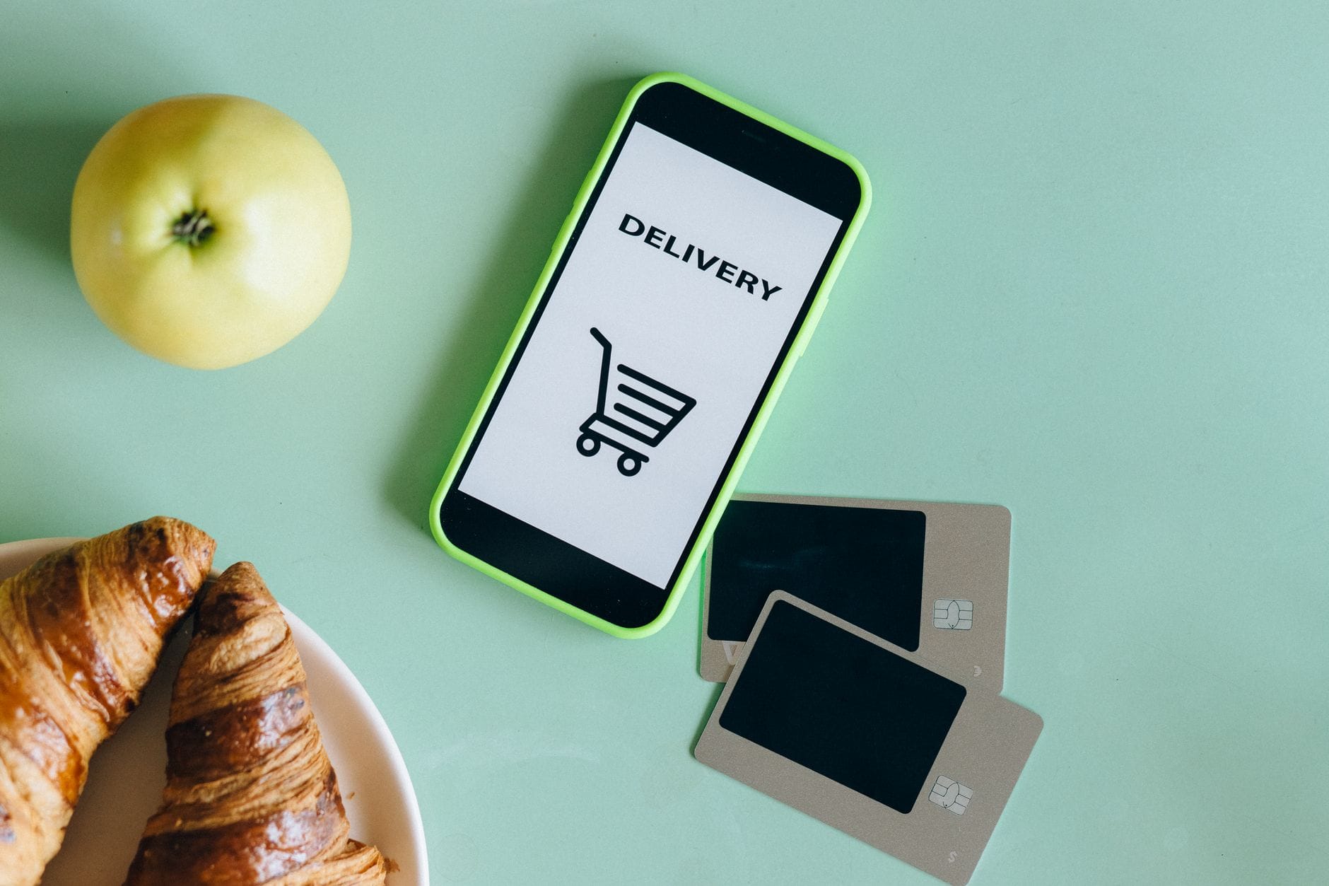 Smartfon z apką dostawy obok rogalików, jabłka i kart płatniczych