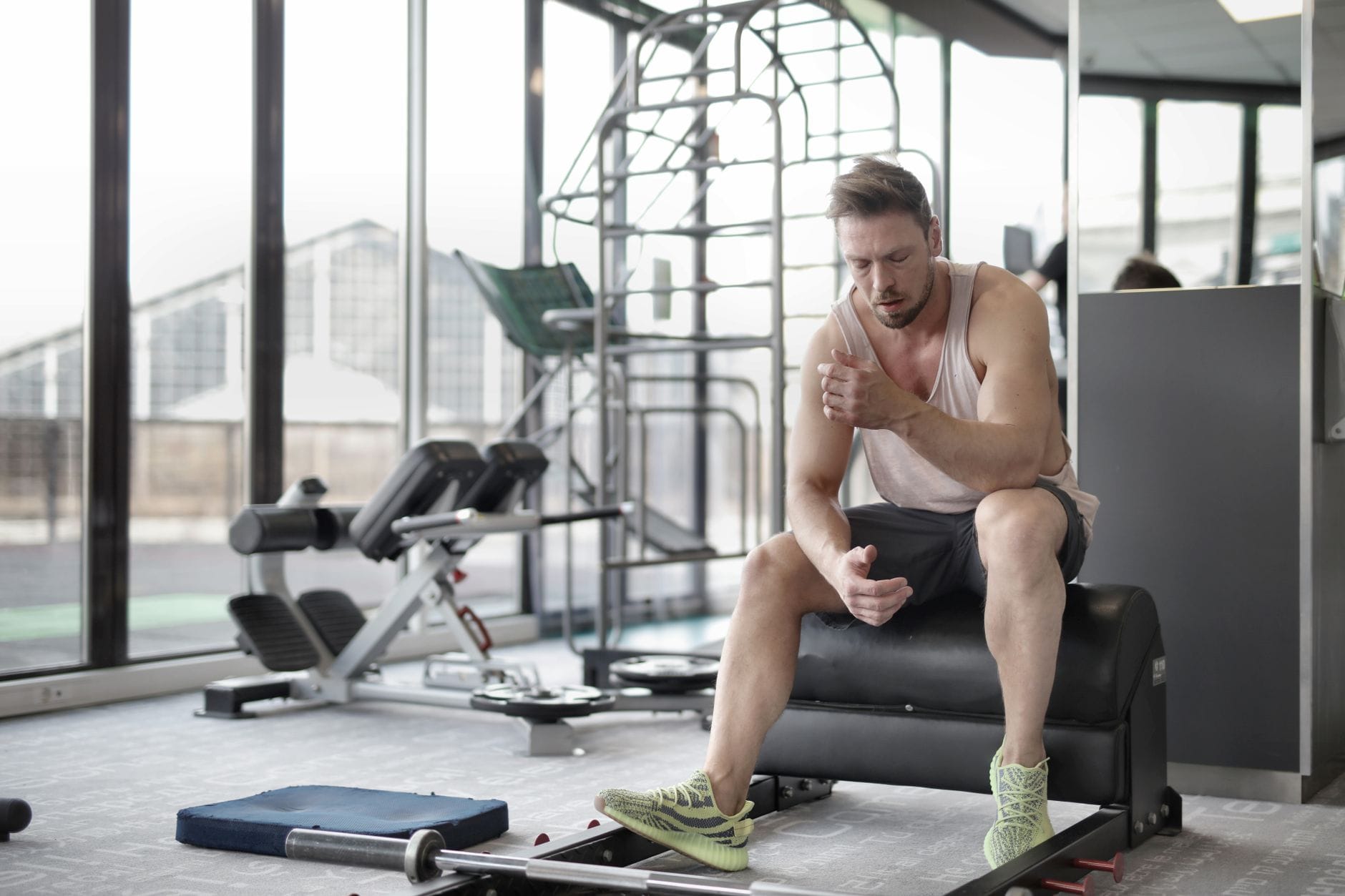 Jak zaplanować domową regenerację po treningu: praktyczny przewodnik z akcesoriami sportowymi Zmęczony młody sportowiec siedzi na ławce w siłowni po treningu