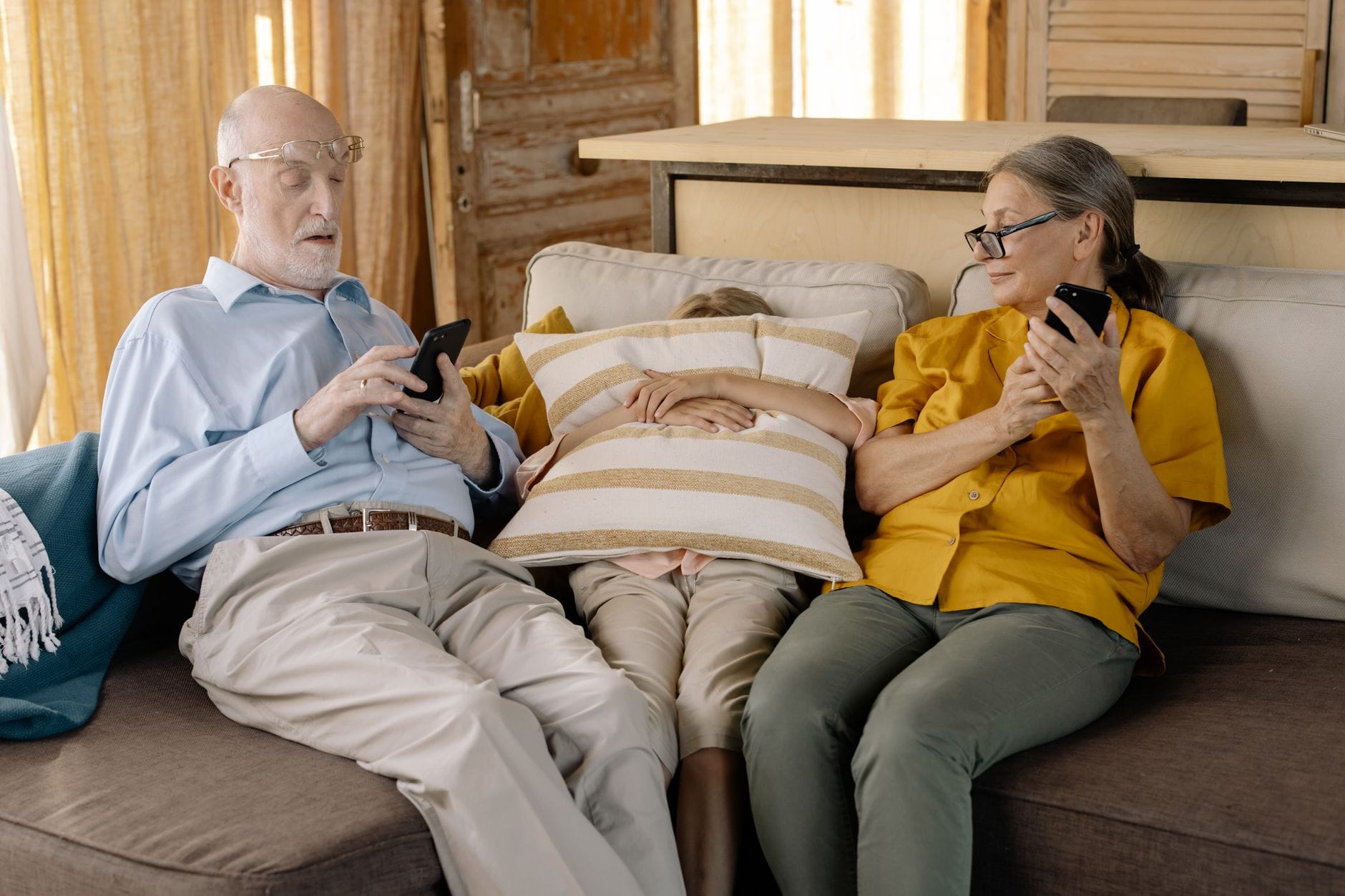 Seniorzy z wnukiem na kanapie korzystają ze smartfonów