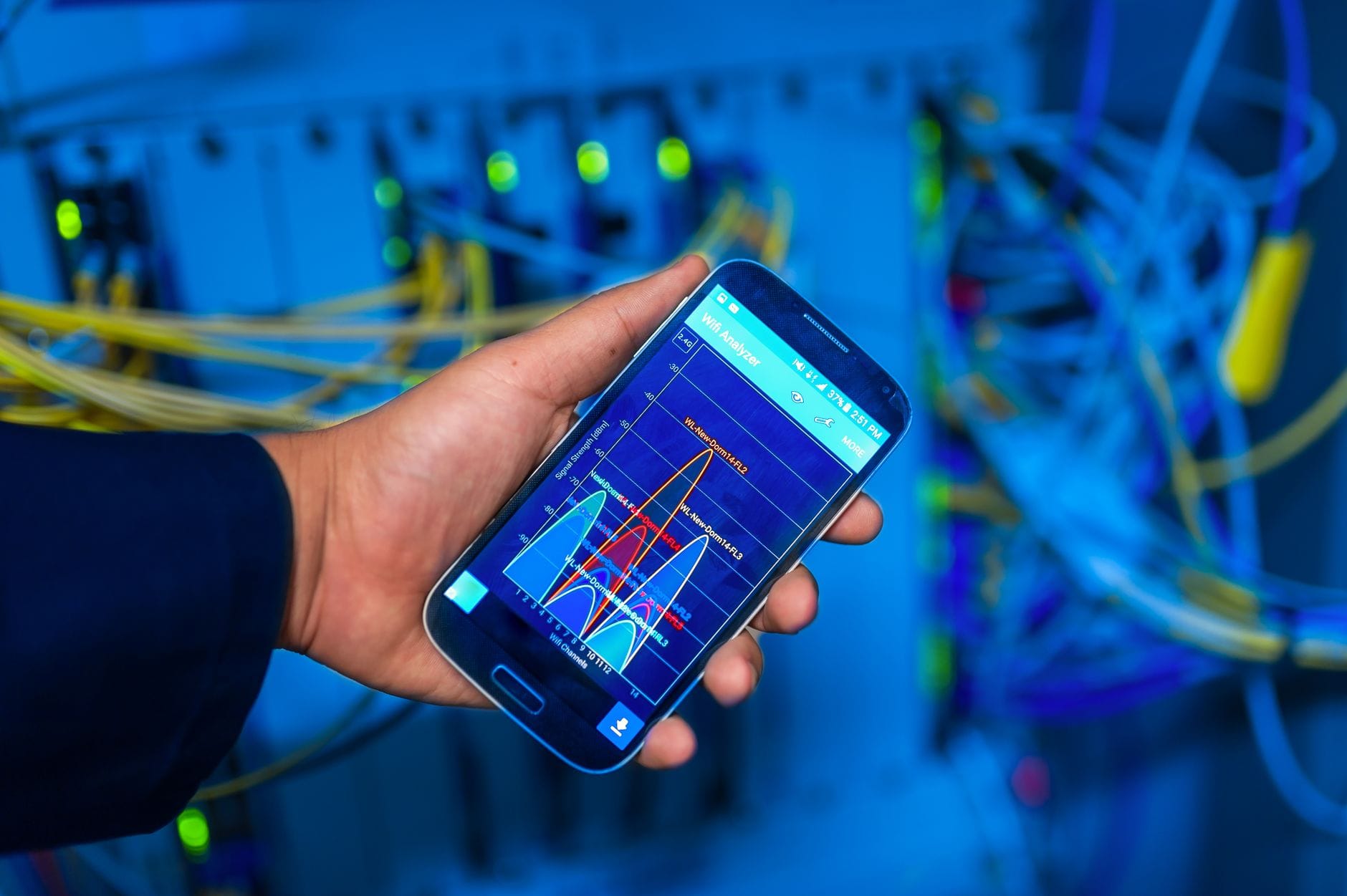 Dłoń trzymająca smartfon z analizą sieci na tle serwerowni