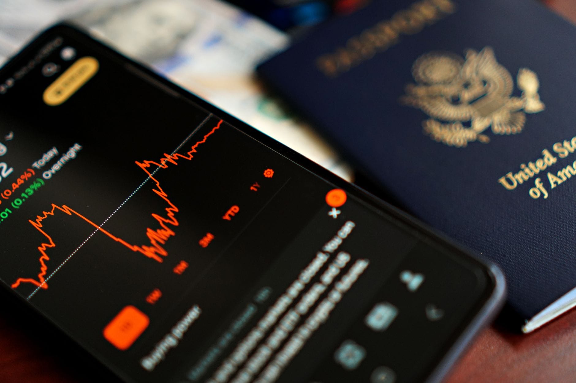 Smartfon z danymi giełdowymi obok paszportu USA na biurku