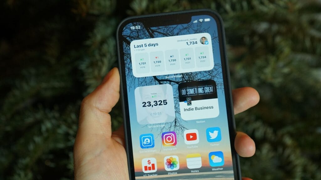 Dłoń trzyma smartfon z widocznymi ikonami aplikacji i widżetami