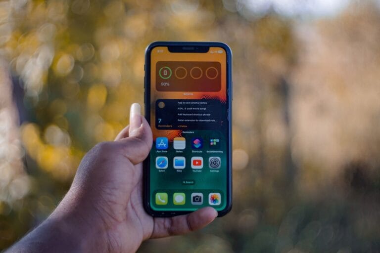 Dłoń trzymająca smartfon z widocznymi aplikacjami na ekranie na zewnątrz